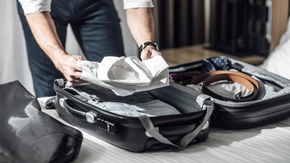 Man putting a folded shirt into luggage.